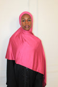Person wearing a bright pink hijab and black outfit on a white background